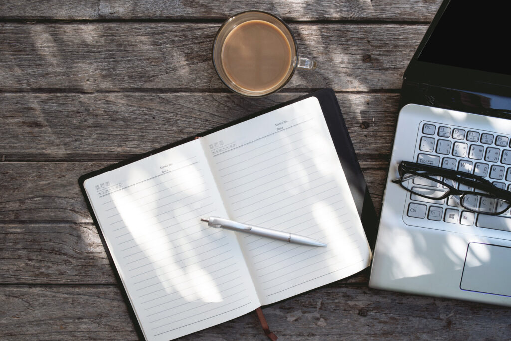 Laptop, notebook, and coffee on a desk for AllSys lesson designer workspace